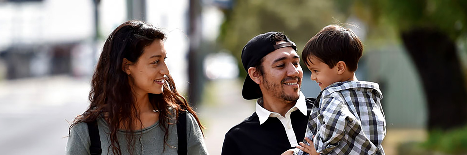 Two smiling adults carrying toddler.