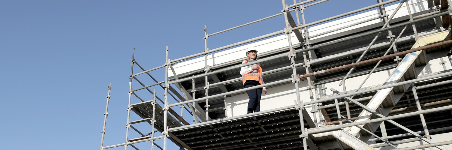 A female building certifier stands on scaffolding at a building site. Credit: NSW Department of Planning and Environment / Christopher Walters