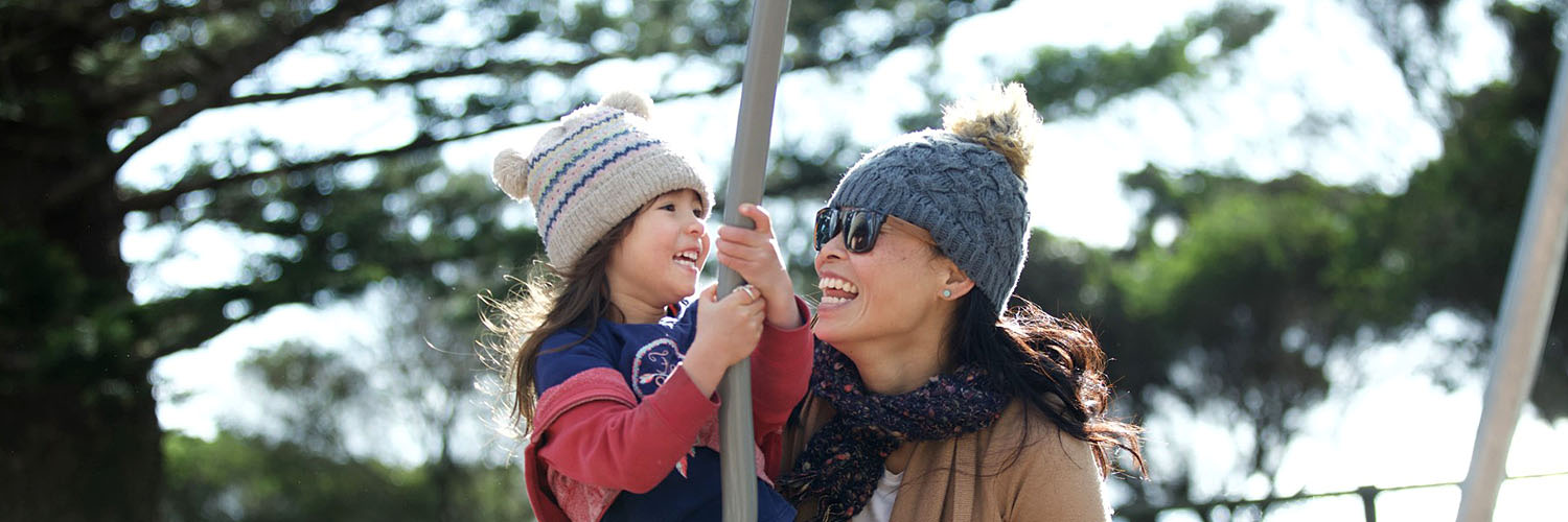 Mother and child laughing and smiling at a playground.