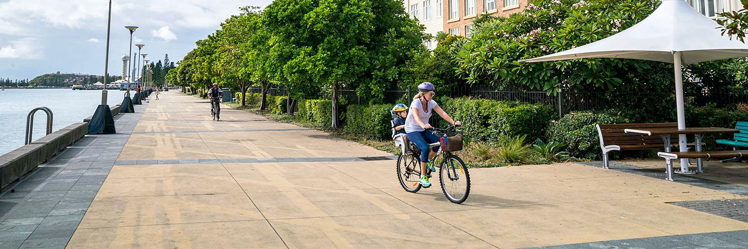 People walk or ride their bicycles along the boardwalk at Honeysuckle Precinct. Newcastle, NSW. Credit: NSW Department of Planning and Environment / Jaime Plaza Van Roon