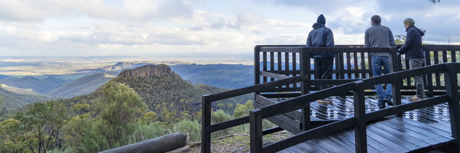 Male tourists look beyond the enormous expanse of Pilliga Scrub to the majestic Warrumbungles from Doug Sky lookout, Mount Kaputar National Park. Credit: Simone Cottrell/DPE