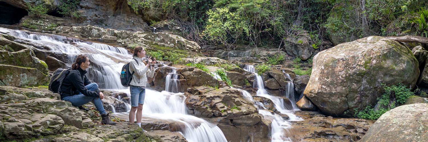 Two people hiking near a small waterfall.