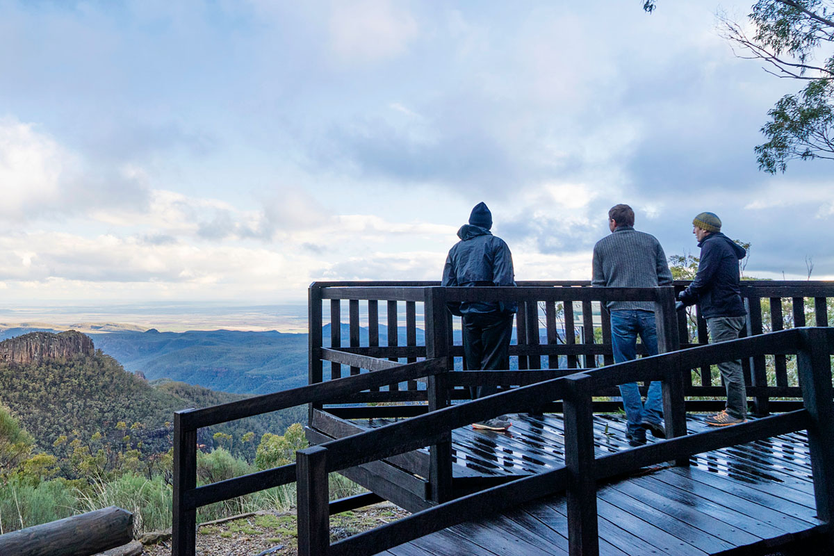 Male tourists look beyond the enormous expanse of Pilliga Scrub to the majestic Warrumbungles from Doug Sky lookout, Mount Kaputar National Park. Credit: Simone Cottrell/DPE