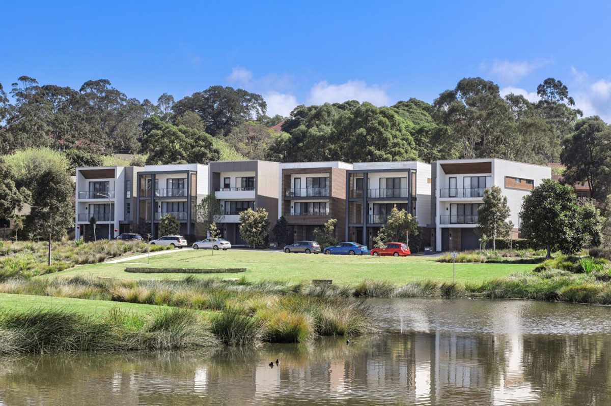 A row of houses next to a lake with trees in the background.