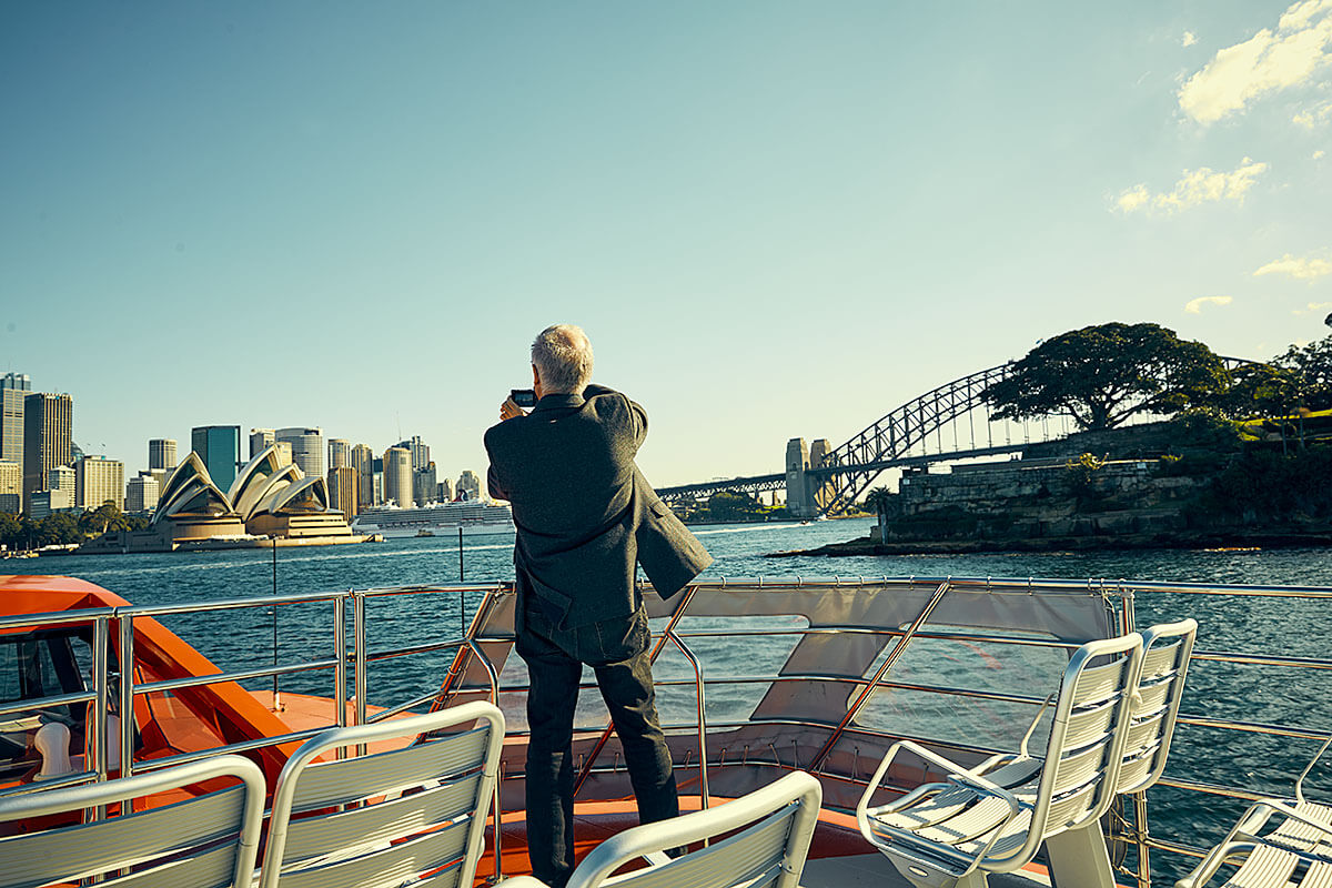 Person on a boat heading towards the Sydney Opera House taking a photograph. Credit: Cory White / Government Architect NSW