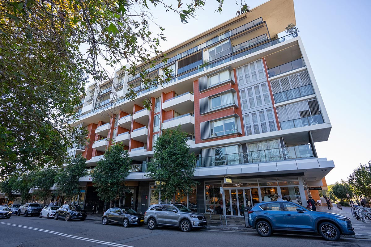 A modern apartment building with several cars parked along a tree-lined street. Credit: Department of Planning, Housing and Infrastructure / Joshua Tredinnick 