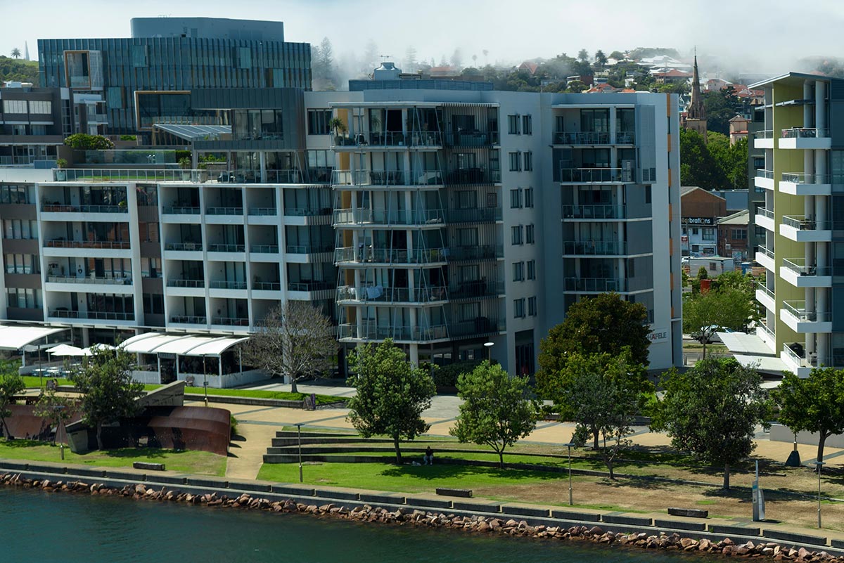 A scenic waterfront featuring several buildings standing on the shore. Credit: Destination NSW